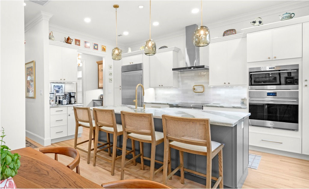 Refined white and gray kitchen with a marble island, cane counter stools and brass pendants